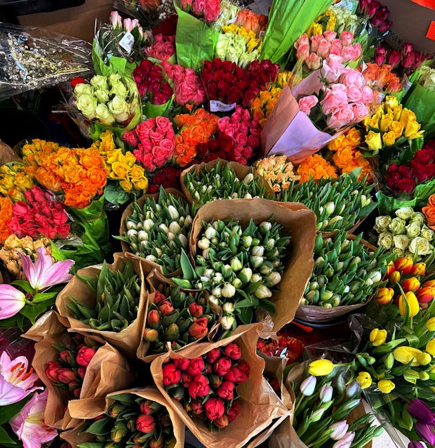 A vibrant display of fresh flowers arranged in bouquets, featuring a variety of blooms such as white tulips, pink roses, red roses, orange and yellow daffodils, and pink and red carnations. The flower